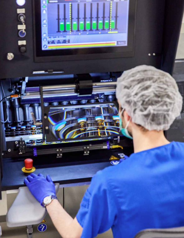 A person in a hair net, mask and blue scrubs looking at a computer